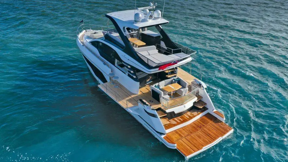 Luxury motor yacht with a spacious deck, lounge area, and dining table, floating on calm turquoise waters.